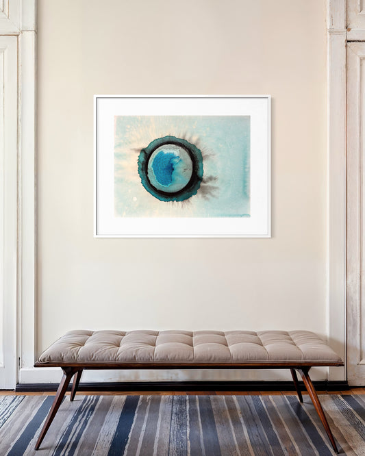 Framed abstract art piece on a wall above a bench with a striped rug